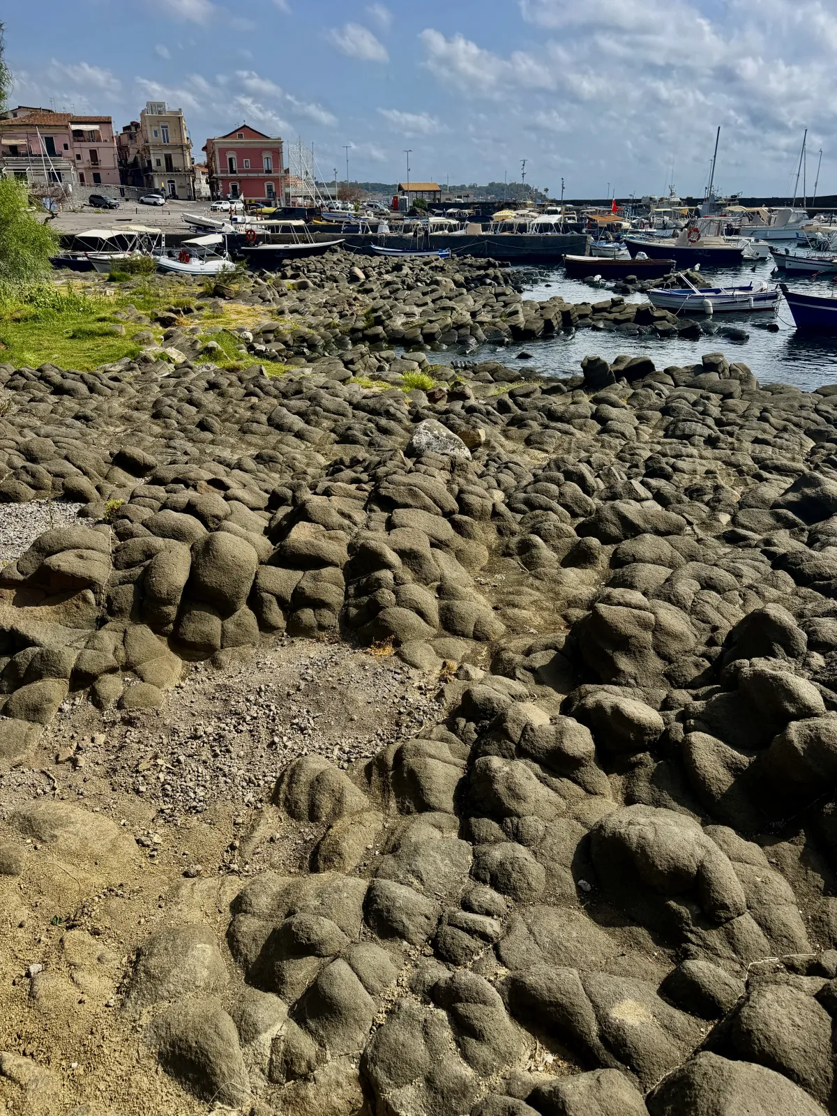 Le testate dei basalti colonnari affioranti nel porto vecchio di Acitrezza, con il paese sullo sfondo