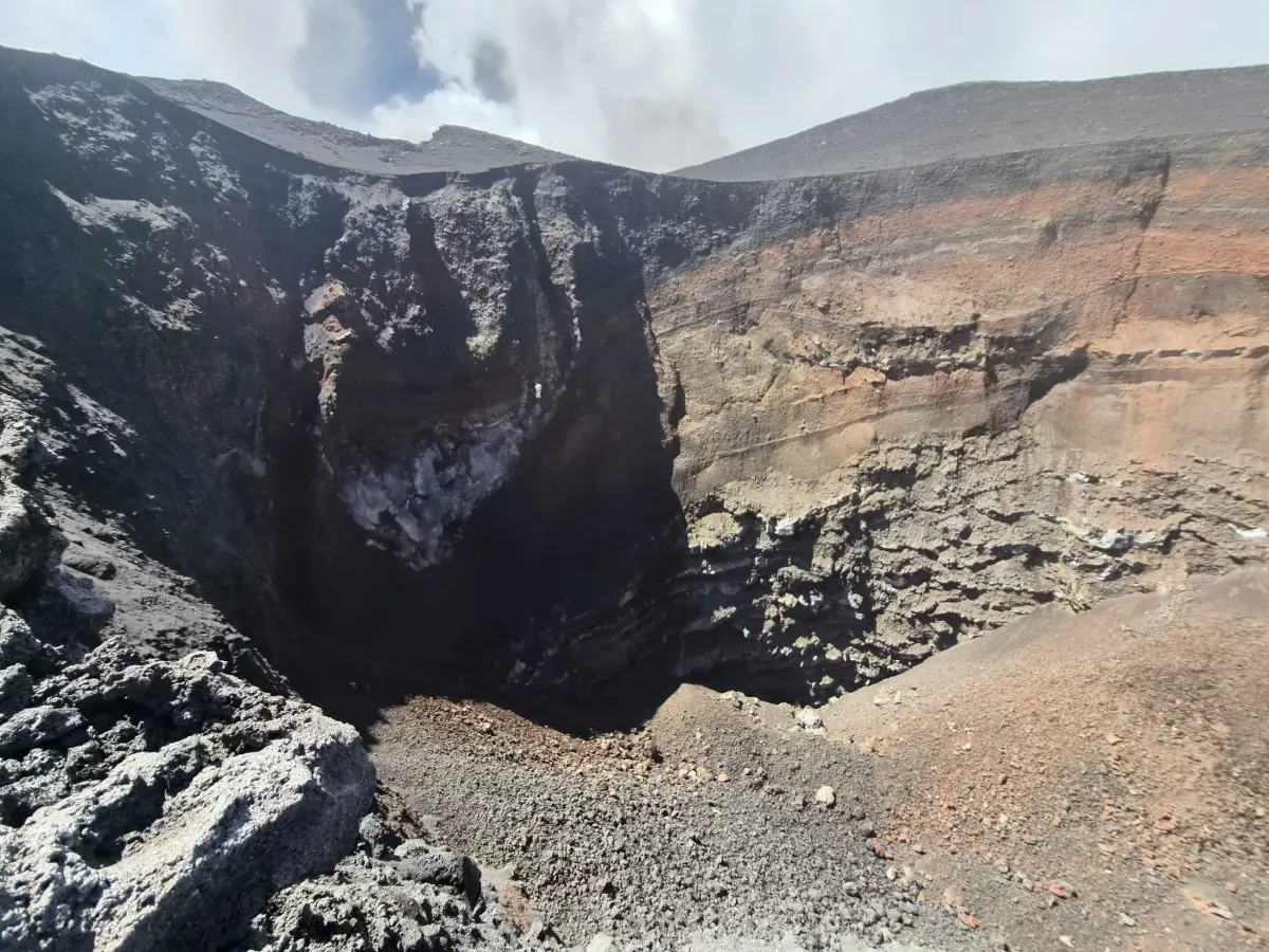 Pit crater sull'Etna visto dall'orlo: pozzo profondo dalle pareti verticali, con il cono che degassa sullo sfondo